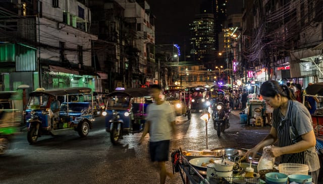 Bangkok street at night, tuk-tuks, tangled wires, food carts, neon, motion blur
