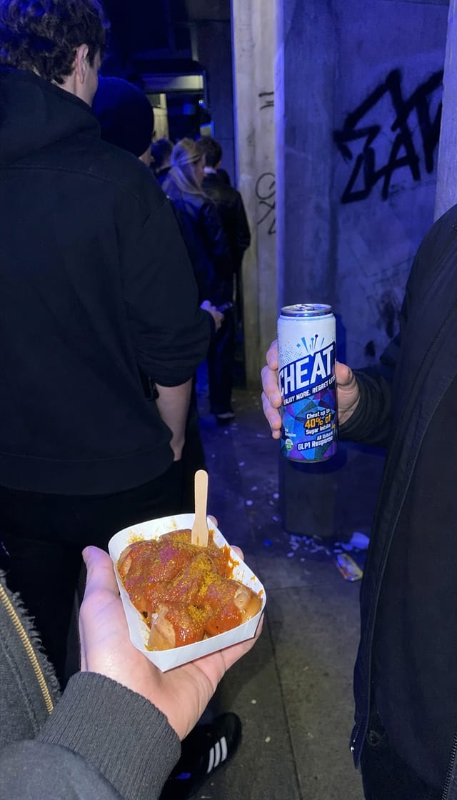Club queue in Berlin at night, concrete, graffiti, people in black, cold blue light, a currywurst tray in someone's hand