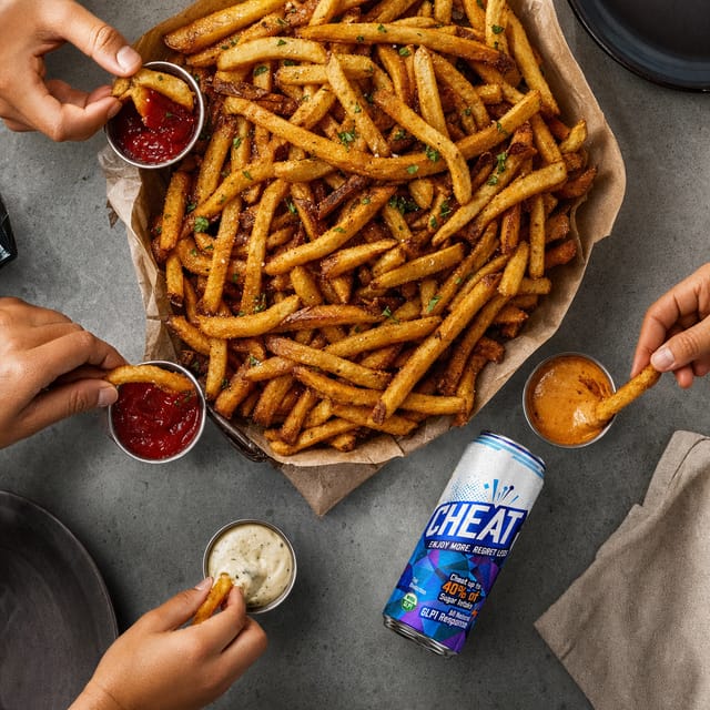 Overhead of a huge pile of fries with dipping sauces in a paper-lined basket