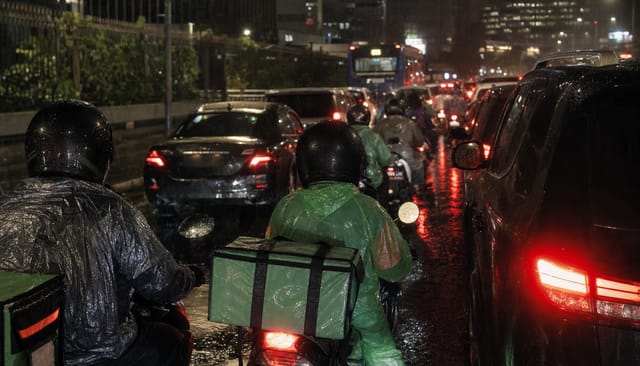 Jakarta traffic at night, motorbike delivery riders with insulated food boxes, rain