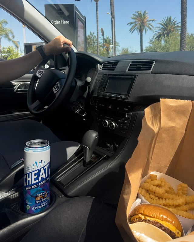 Fast-food drive-through order in a car, a paper bag of burgers and fries on the passenger seat, dashboard, palm trees through the windshield