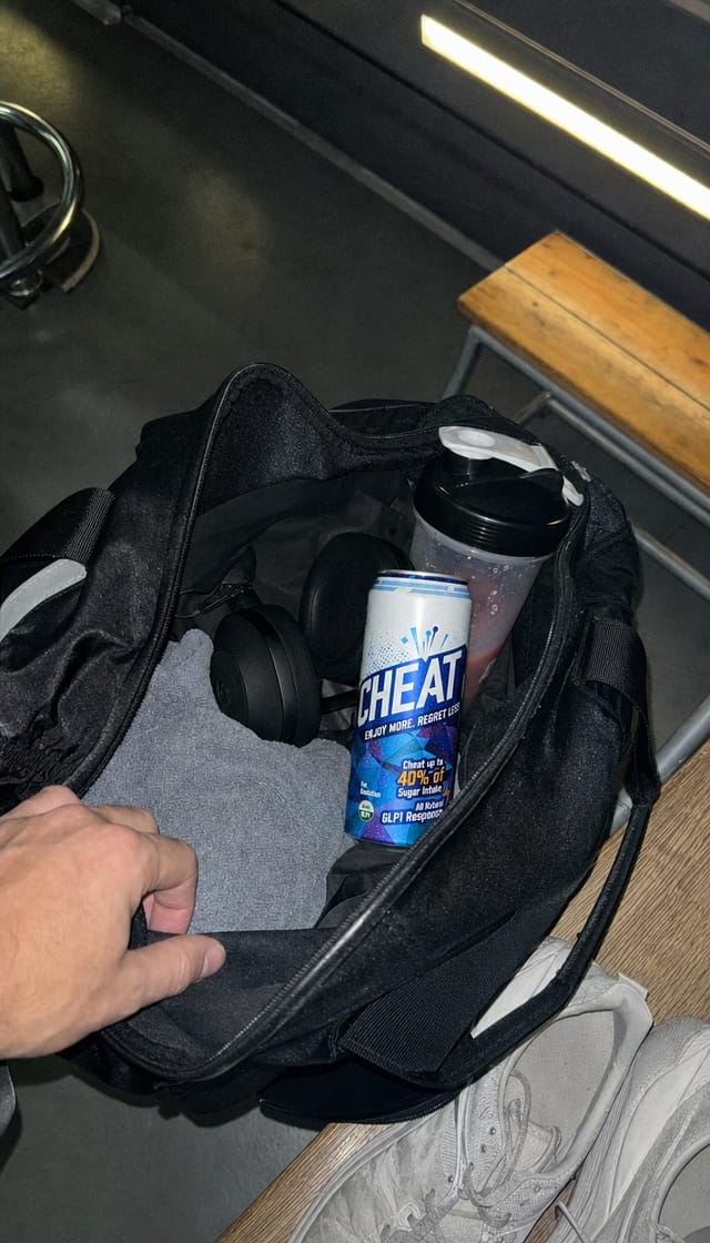 Gym bag open on a locker room bench, towel, headphones, shaker bottle, sneakers, fluorescent light