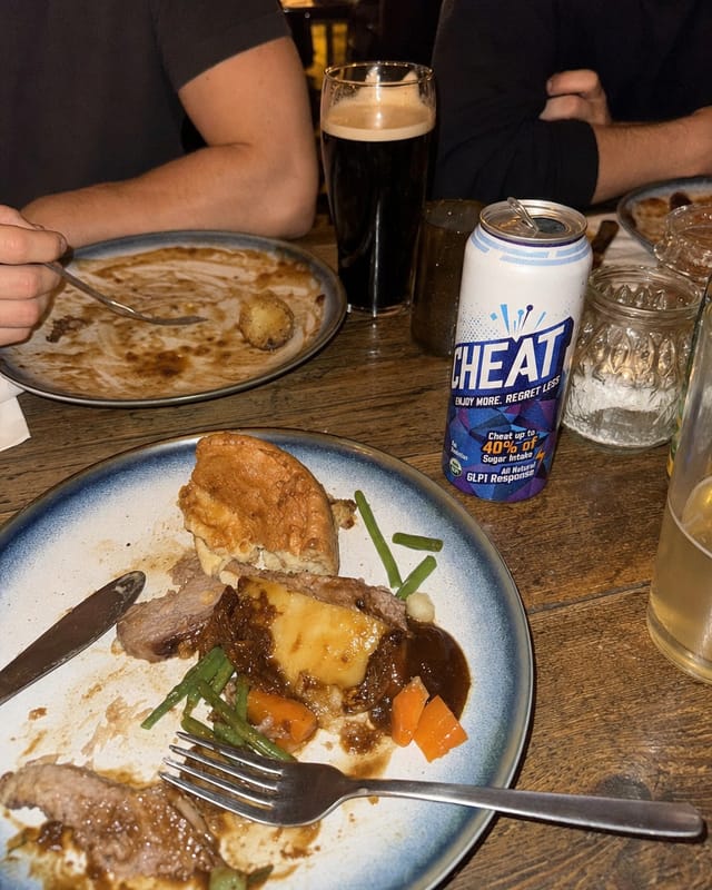 A pub table with a Sunday roast half eaten, wooden table, dim warm light, friends' arms
