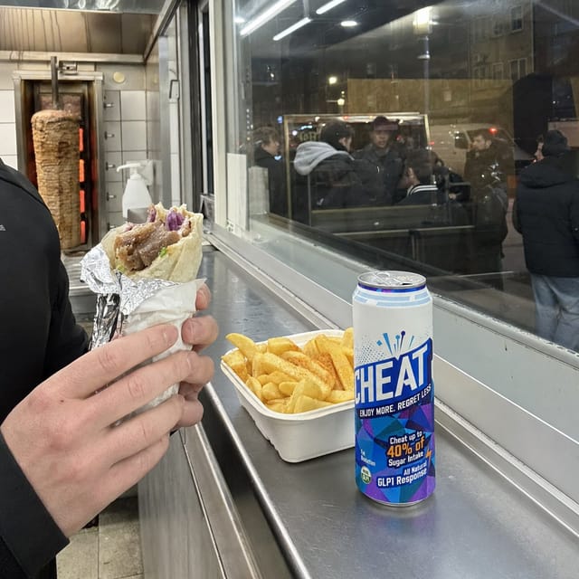 Late-night kebab shop counter in London, doner wrap in foil, chips, fluorescent light, a queue reflected in the glass