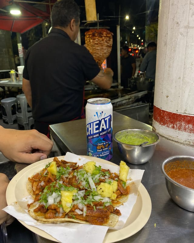 Mexico City taco stand at night, a plate of tacos al pastor with pineapple, salsa bowls, plastic stools, street