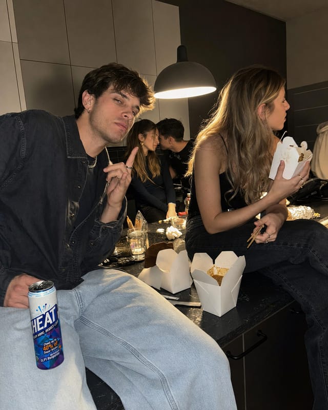 An after-party kitchen at 4am, people sitting on the counter, takeaway boxes, one lamp