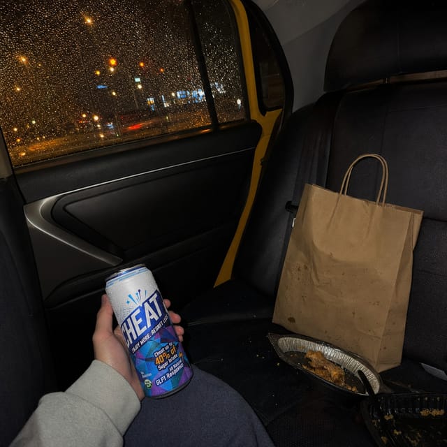 Back seat of a yellow taxi at night, rain on the window, city lights, a takeaway bag on the seat
