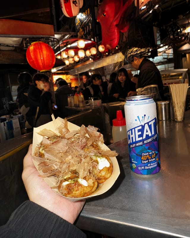 Osaka street food stall at night, a paper tray of takoyaki with bonito flakes moving in the heat, dense lantern signage, crowd behind