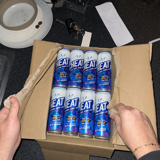 Top-down phone photo of two hands ripping open a plain brown cardboard case on a cluttered kitchen counter, keys and a takeaway receipt near