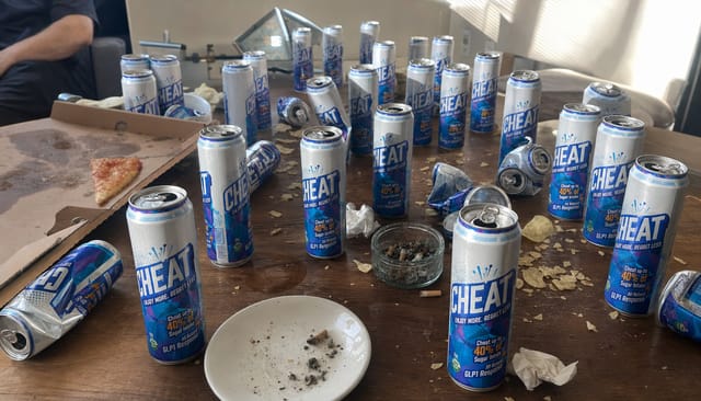 Morning-after party table covered with empty and half-full cans, crushed chips, a pizza box with one slice left, cigarette ash, sticky rings