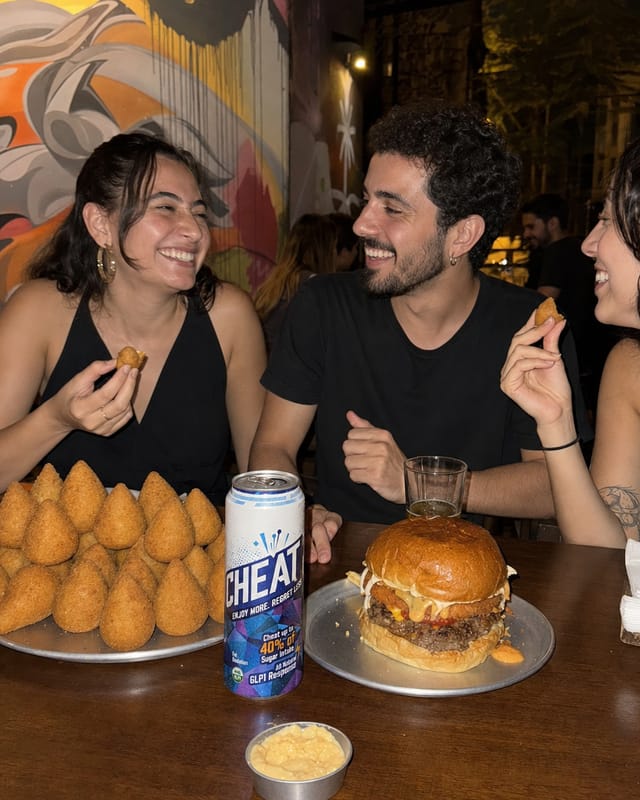 São Paulo bar table at night with a stack of coxinhas and a big burger, friends, warm light, graffiti wall