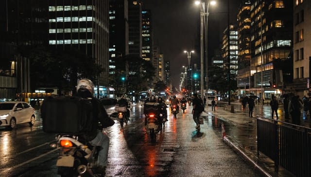 São Paulo avenue at night, dense towers, motorcycle couriers, wet streets