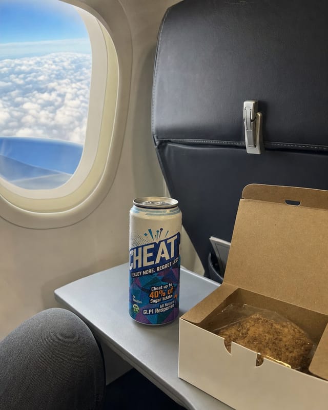 Airplane tray table with a snack box, window seat, clouds outside, cramped seat, phone photo