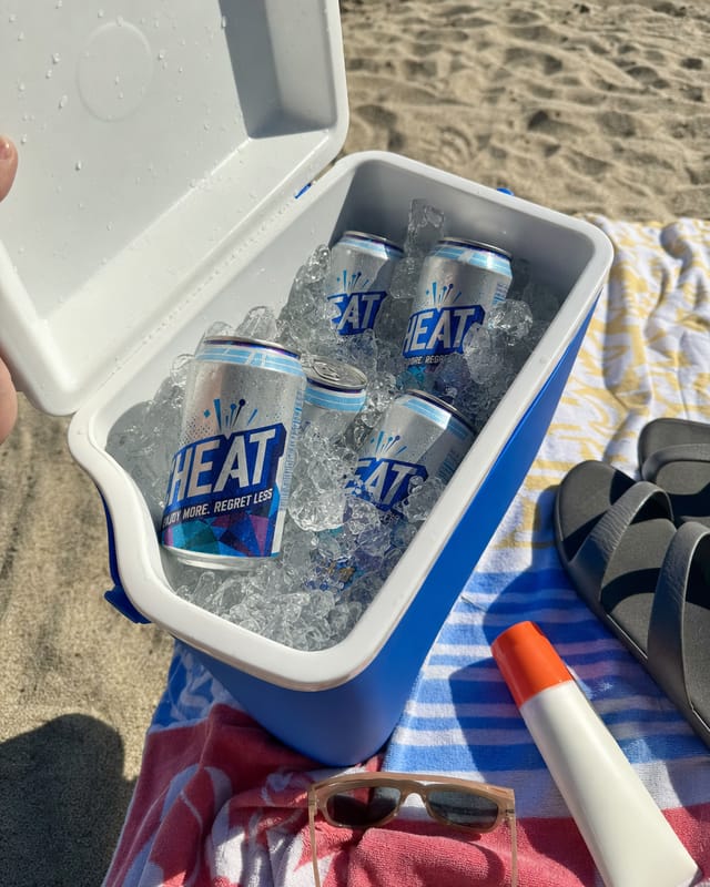 An open cooler full of ice on a beach towel, sunscreen, flip flops, bright sun