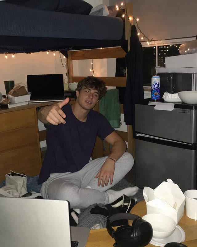 Messy college dorm room, bunk bed, a plain laptop with no logo, takeaway containers, string lights, a mini fridge