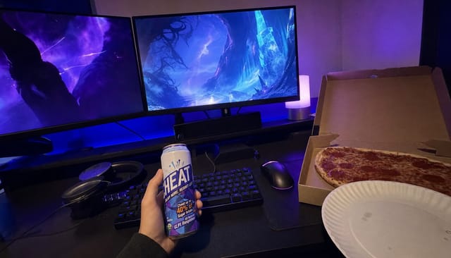 A gaming desk at night with RGB lighting, two monitors showing abstract game visuals with no text, mechanical keyboard, a pizza box open on